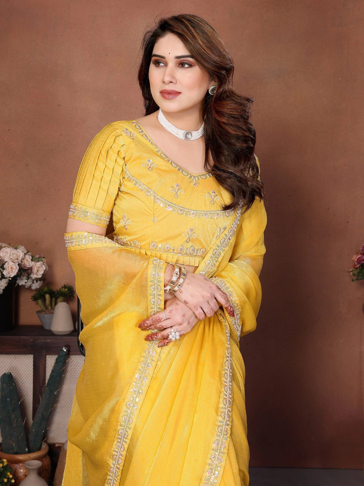 Woman in a yellow saree with intricate designs against a brown background